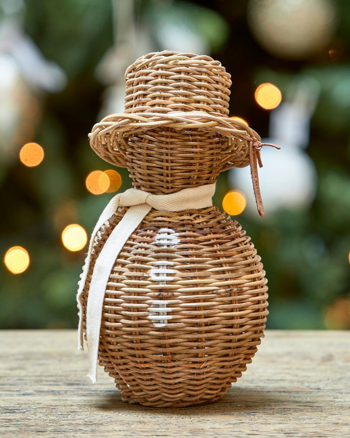 Großer Rustic Rattan Schneemann von Rivièra Maison dekorativ vor einem Weihnachtsbaum mit Lichterketten arrangiert.