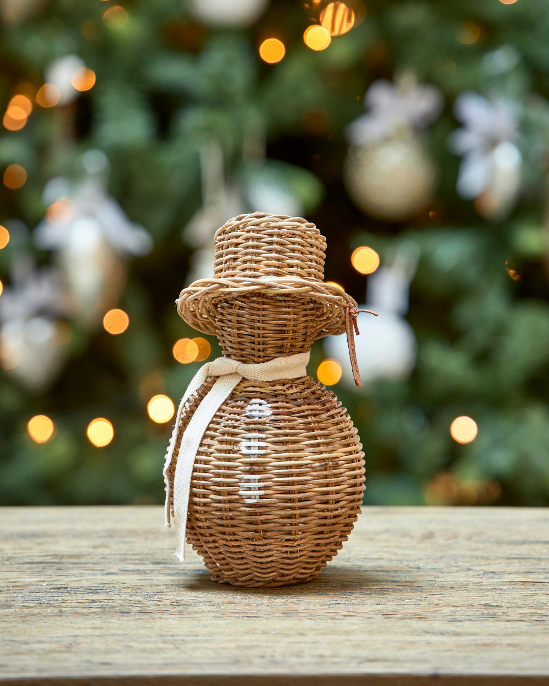 Kleiner Rustic Rattan Schneemann von Rivièra Maison dekorativ vor einem Weihnachtsbaum mit Lichterketten arrangiert.