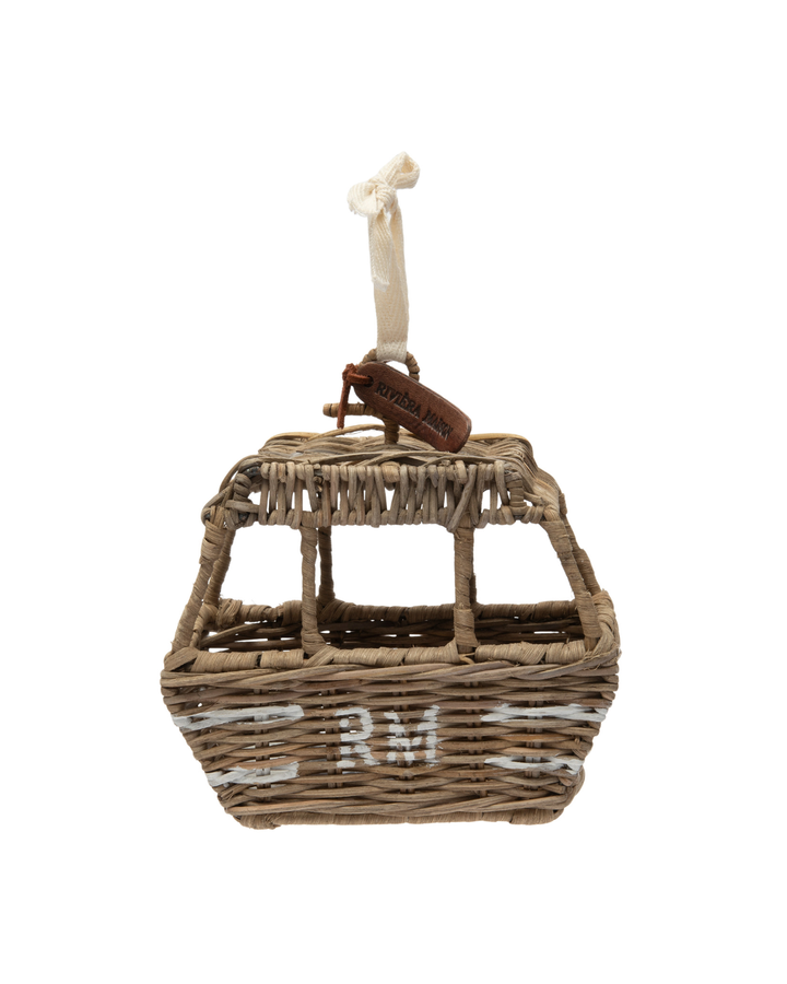 Rustic Rattan Ski Lift Ornament von Rivièra Maison vor weißem Hintergrund, geflochtene Rattan-Gondel mit Stoffband und kleinem braunen RM-Lederetikett.