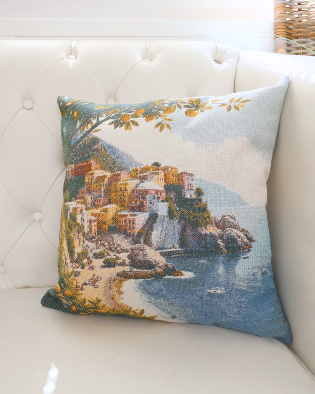 Bild des "Positano" von Sander. Das Motiv besteht aus einer schönen farbvollen Küste und einem Zitronenbaum im Vordergrund. Das Kissen liegt auf einem weißen Sofa.