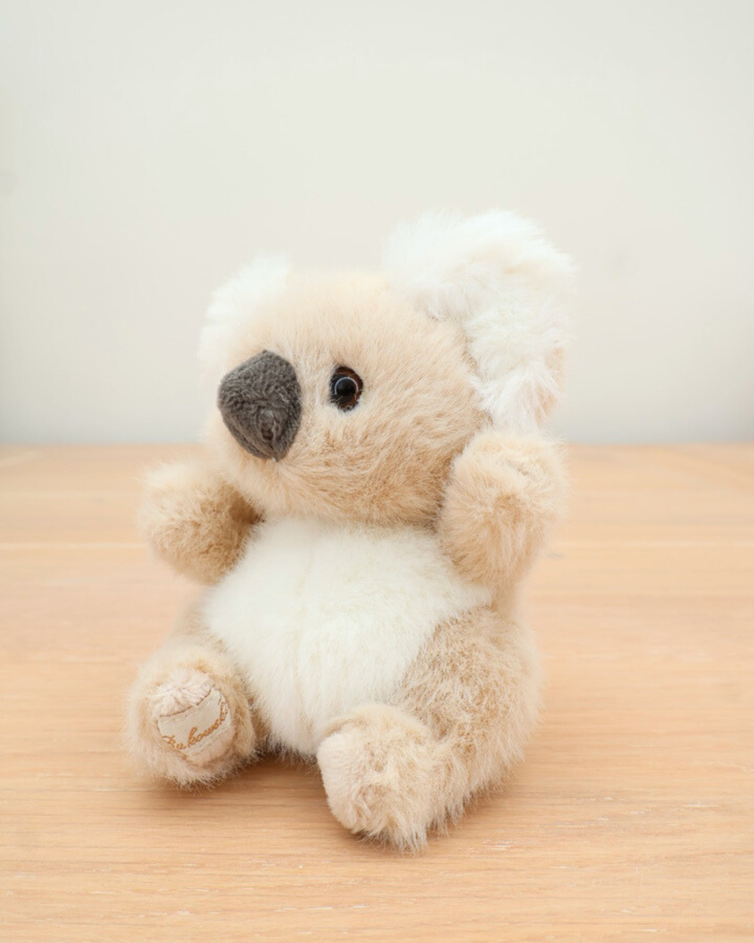 Der Baby-Koala Schlüsselanhänger von Bukowski sitzt auf einem Holztisch. Sein freundliches Gesicht und die weichen Pfoten sind im Detail zu sehen.