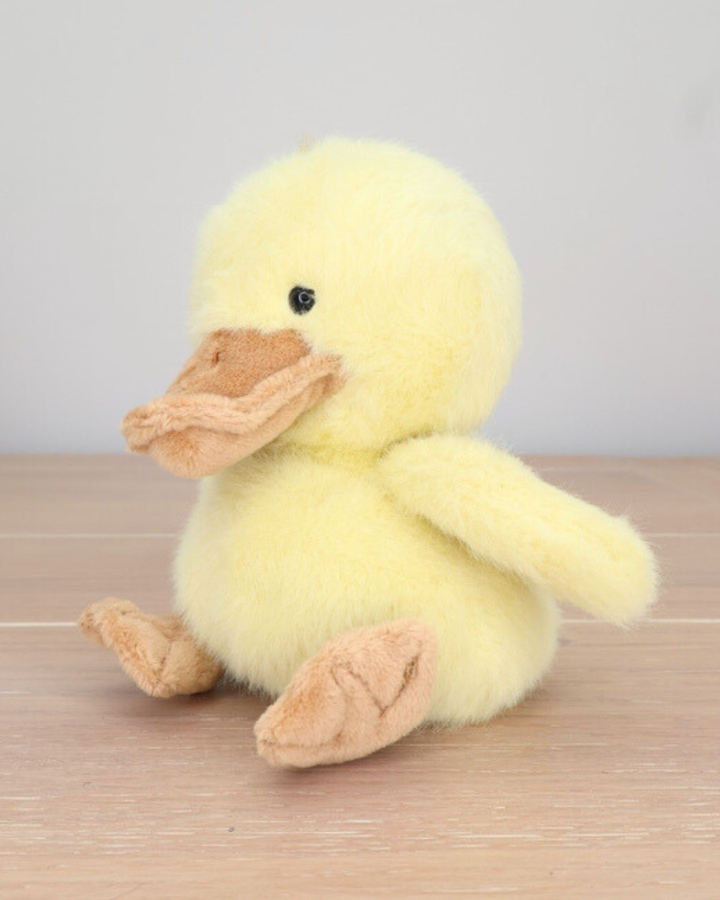 Ein gelbes Entenküken Kuscheltier von Bukowski sitzt auf einem Holzboden.