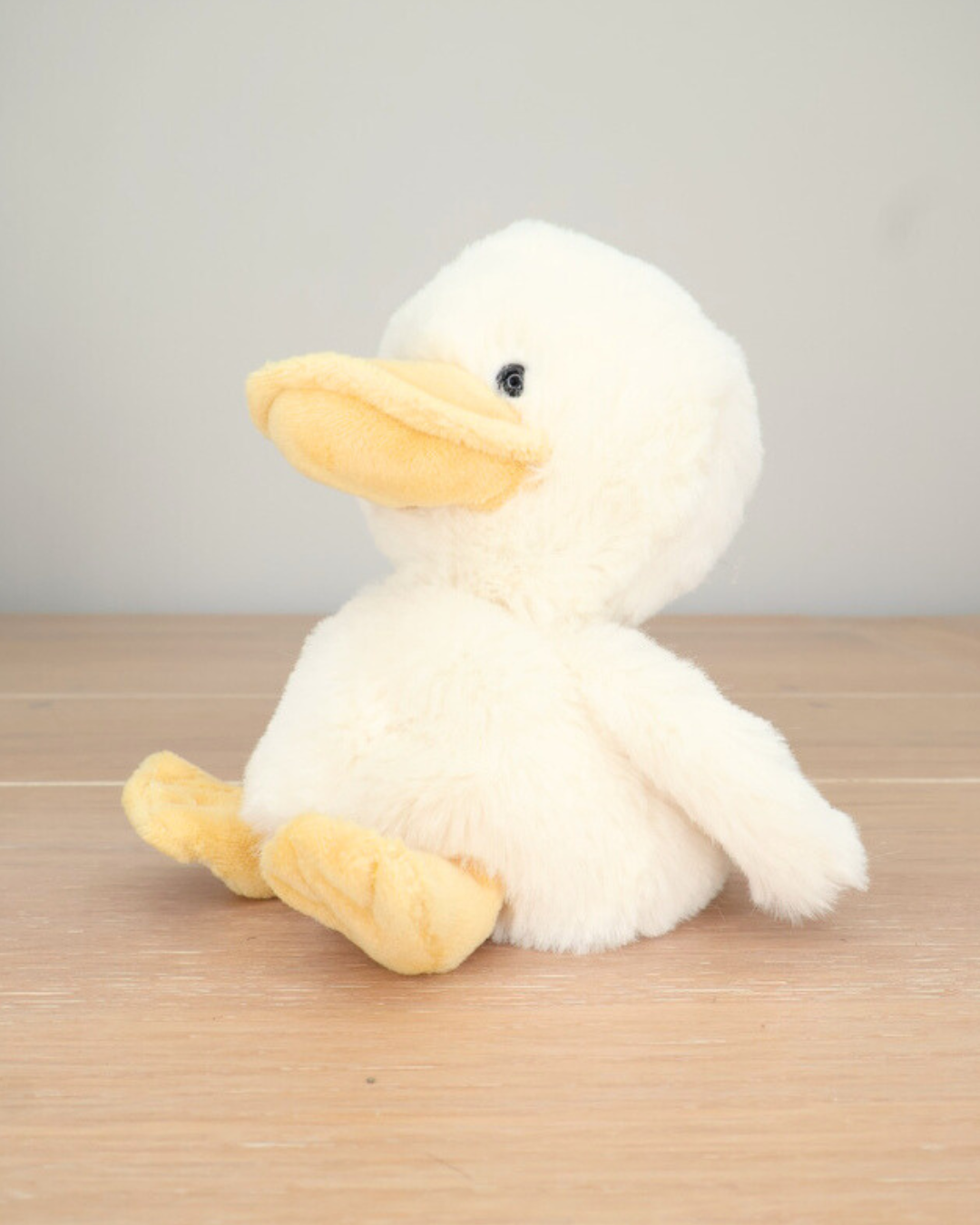 Ein weißes Entenküken Kuscheltier von Bukowski sitzt auf einem Holzboden.