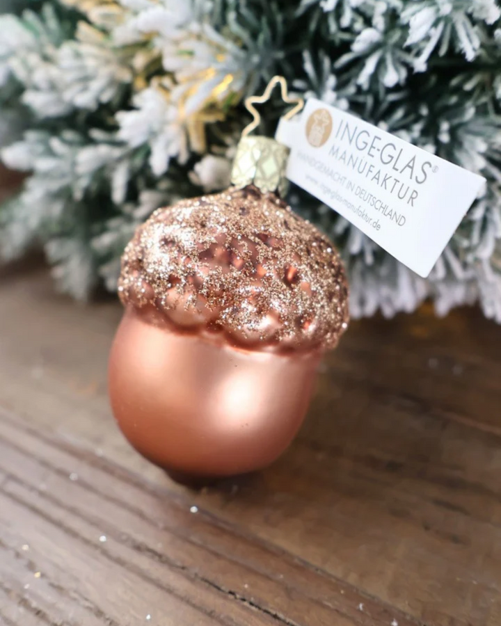 Schräge Ansicht des großen weihnachtlichen Eichel Ornaments von Inge Glas, welches vor weiß gepudertem Tannengrün auf einem Holztisch dekoriert ist.