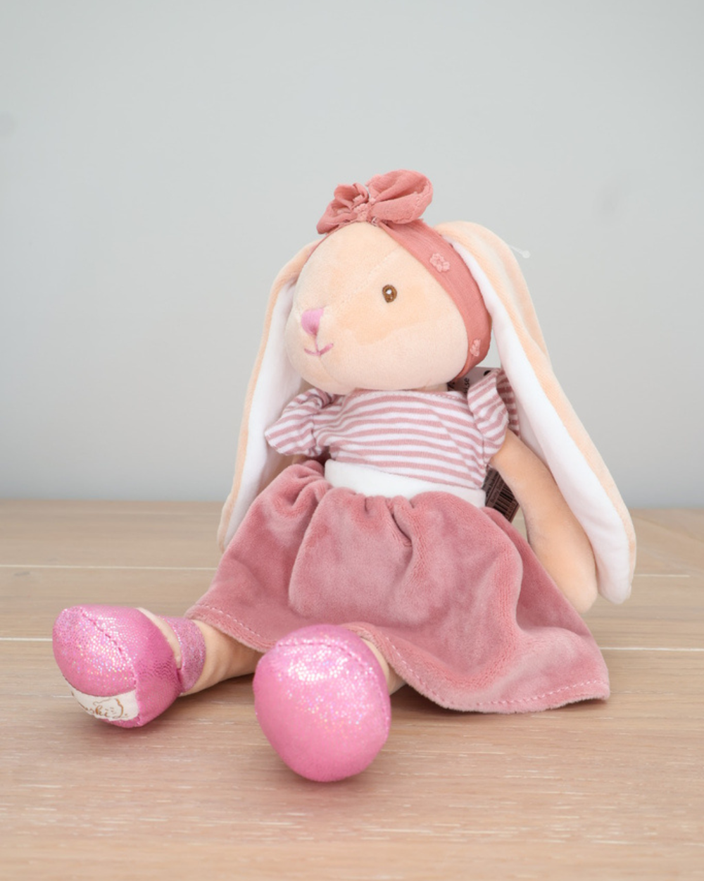 Ein Hase mit rosafarbenem Kleid und pinken Glitzer-Schuhen von Bukowski sitzt auf einem Holzboden.