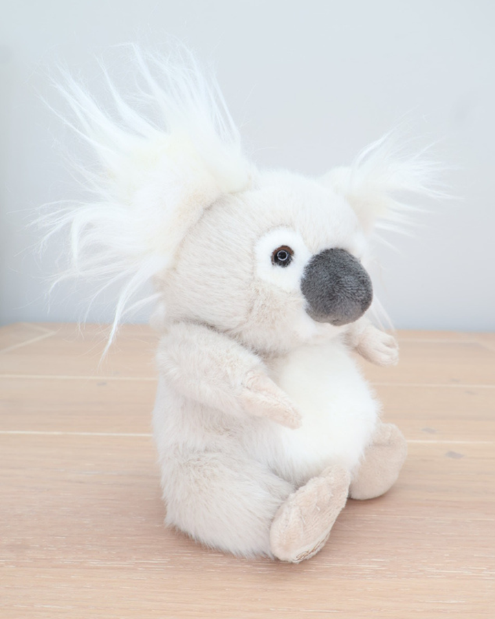 Seitenansicht des Baby Koalas von Bukowski. Der Koala sitzt auf einem Holzboden, die flauschigen Ohren und der weiche Fellcharakter sind gut sichtbar.