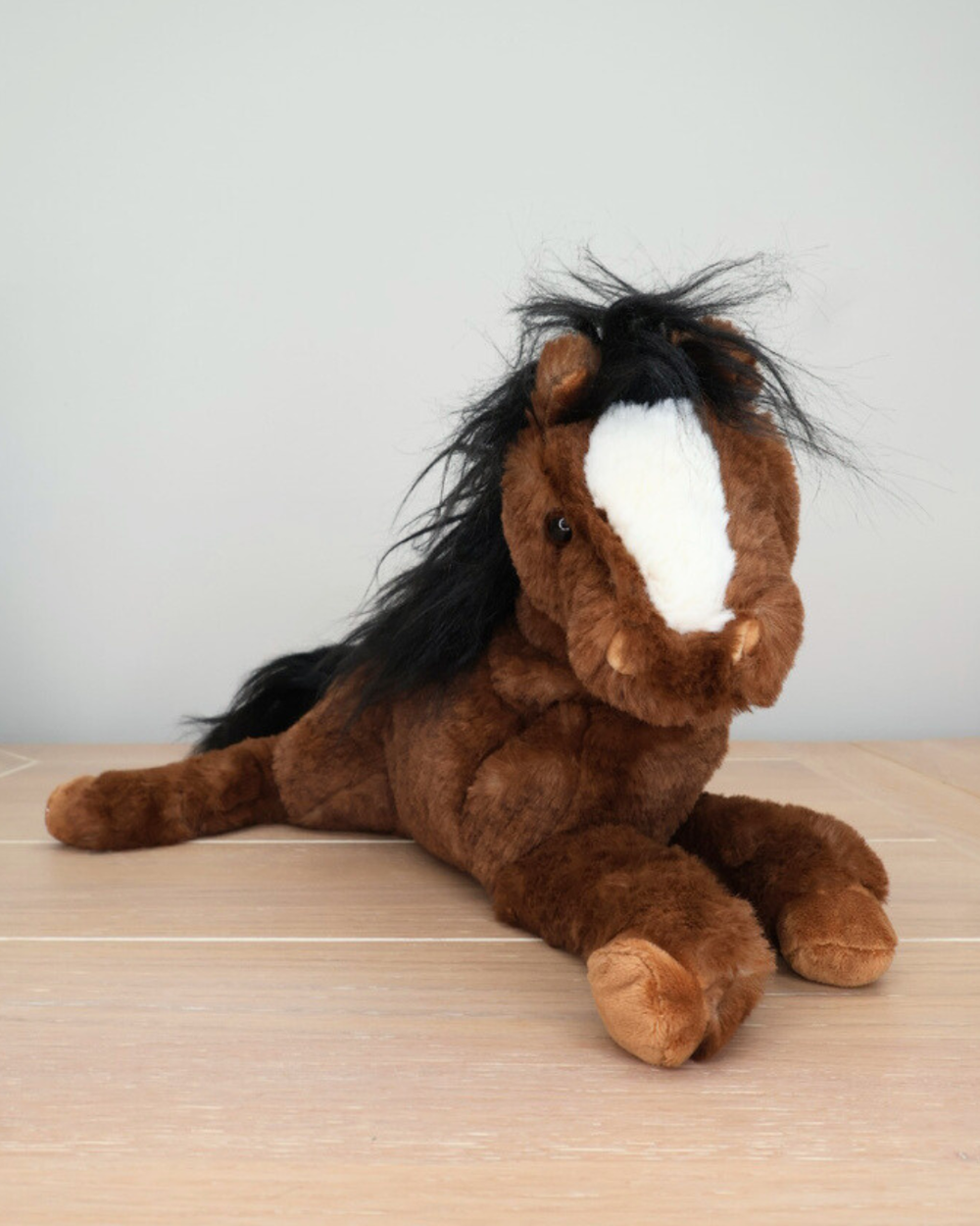 Ein braunes Pferd Kuscheltier mit schwarzer Mähne von Bukowski liegt auf einem hellen Holztisch.