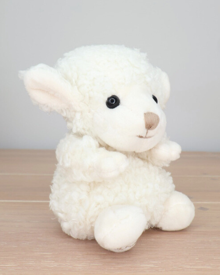 Ein weißes Schaf Kuscheltier mit schwarzen Augen von Bukowski sitzt auf einem hellen Holzboden.