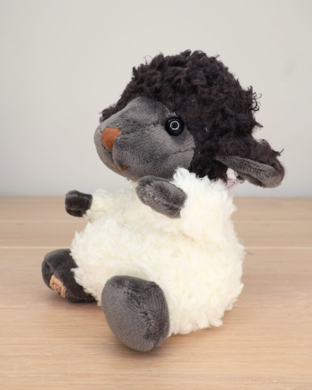 Ein schwarzes Schaf Kuscheltier von Bukowski sitzt auf einem hellen Holzboden.