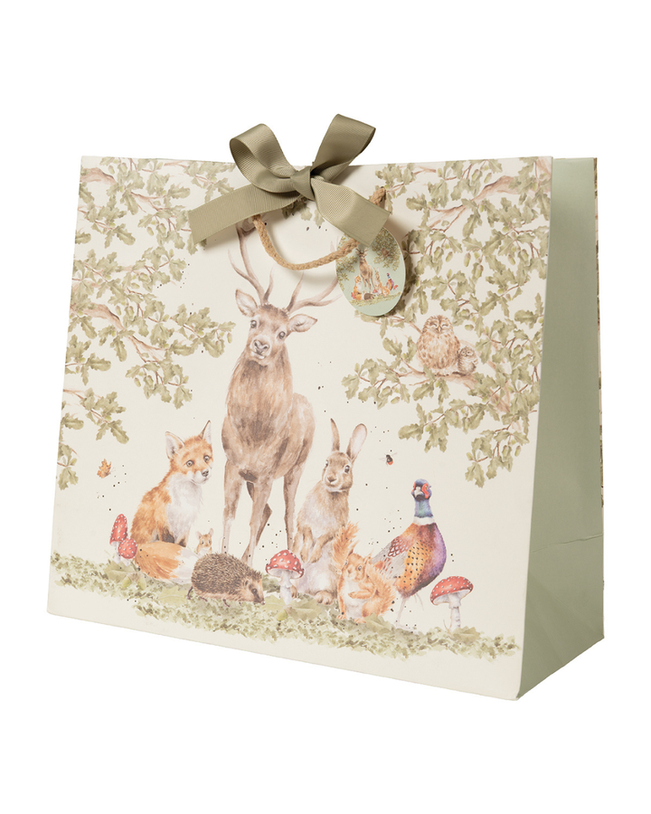 Schrägansicht auf die Geschenktasche The Woodland Clearing. Diese zeigt die Bewohner des Waldes im typisch-natürlichen Stil von Hannah Dale. Hirsch, Fuchs, Hase, Igel, Eichhörnchen, Maus und Fasan stehen unter Eichenbäumen und Zweigen. In der Eiche selbst sitzt ein niedlicher Kauz mit noch süßerem Nachwuchs. Das detailreiche Motiv wird durch Insekten, wie Hummel und Schmetterling, sowie Eicheln und Fliegenpilze vervollständigt.