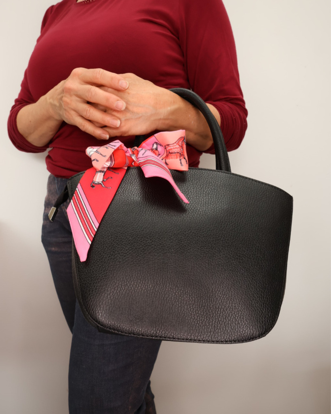 Schwarze Handtasche aus Leder Lotte vom Südstrand mit pinken Bandana seitlich getragen vor weißen Hintergrund.