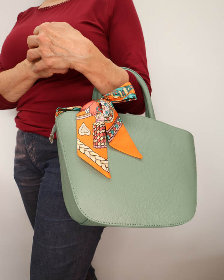 Seegrüne Handtasche aus Leder Lotte vom Südstrand mit pinken orangenem Bandana seitlich getragen vor weißen Hintergrund.