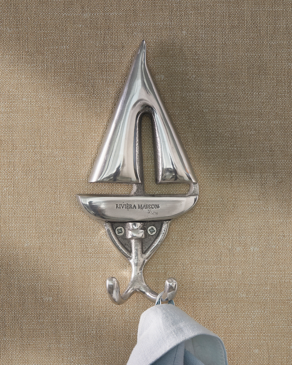 Silberner Segelboot-Haken von Rivièra Maison an einer beigen Wand mit Handtuch.