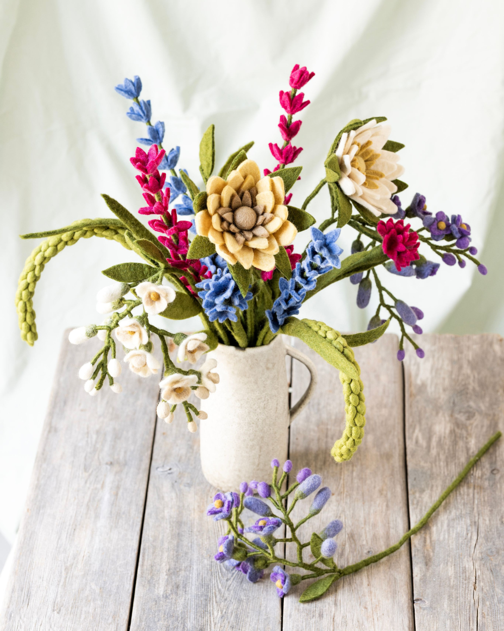 Sommerlicher Blumenstrauß aus Filzblumen von Gry & Sif mit Lupinen, Kornblumen, Sonnenblume und weiteren Blüten in einer hellen Vase auf Holztisch.