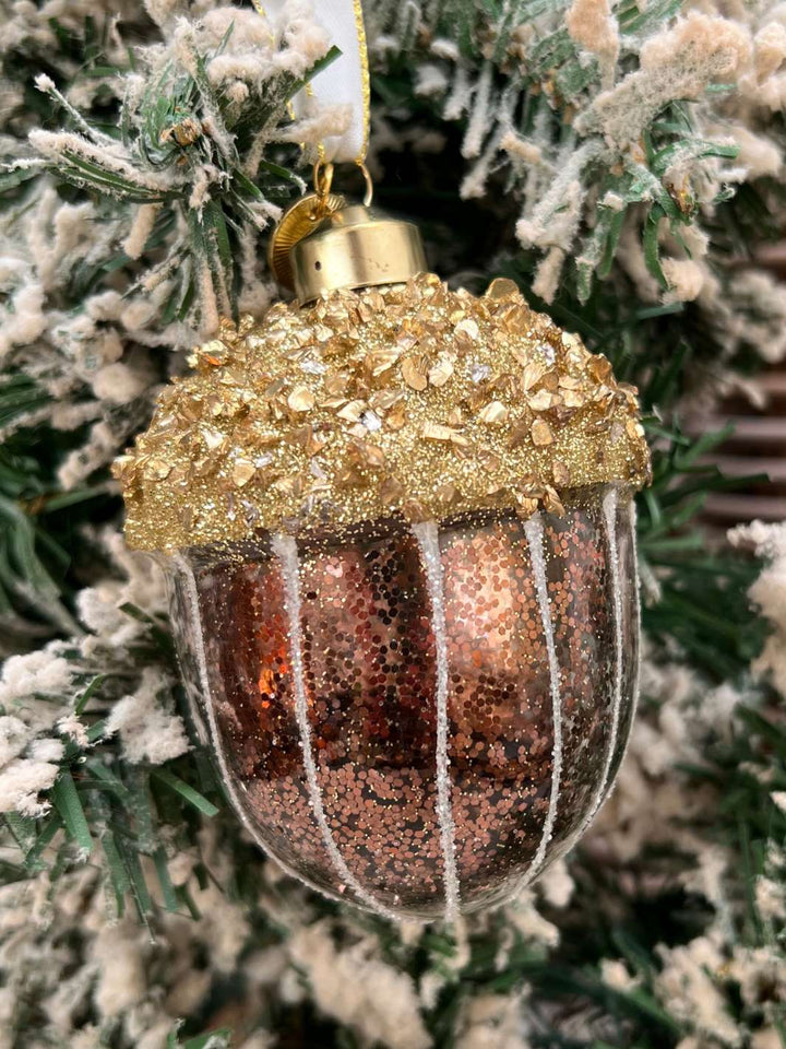 Eichel Weihnachtsbaumanhänger Sparkling Acorn Ornament von Rivièra Maison in braun und gold mit viel Glitzer an einem mit Kunstschnee bedecktem Tannenbaum.