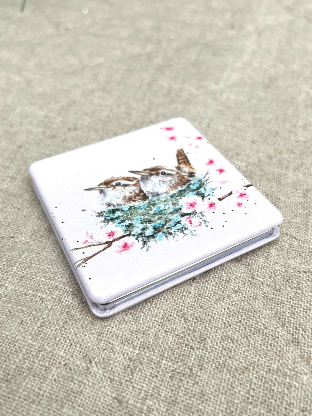 Verpackter kompakter Taschenspiegel mit Zaunkönig-Motiv von Wrendale Designs. Zwei Zaunkönige sitzen in einem Nest mit blühenden Zweigen auf der Verpackung.