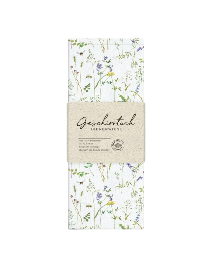 Ein weißes Baumwoll-Geschirrtuch mit Bienenwiesen-Motiv, detailreich mit Blüten, Halmen und Bienen noch verpackt.