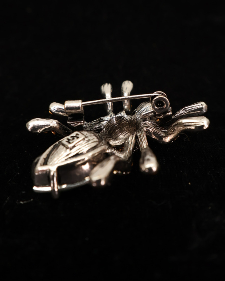 Silberne Rückseite der Spinnen Brosche "Elegant Spider" von Giuno auf schwarzer leicht glitzernder Decke.