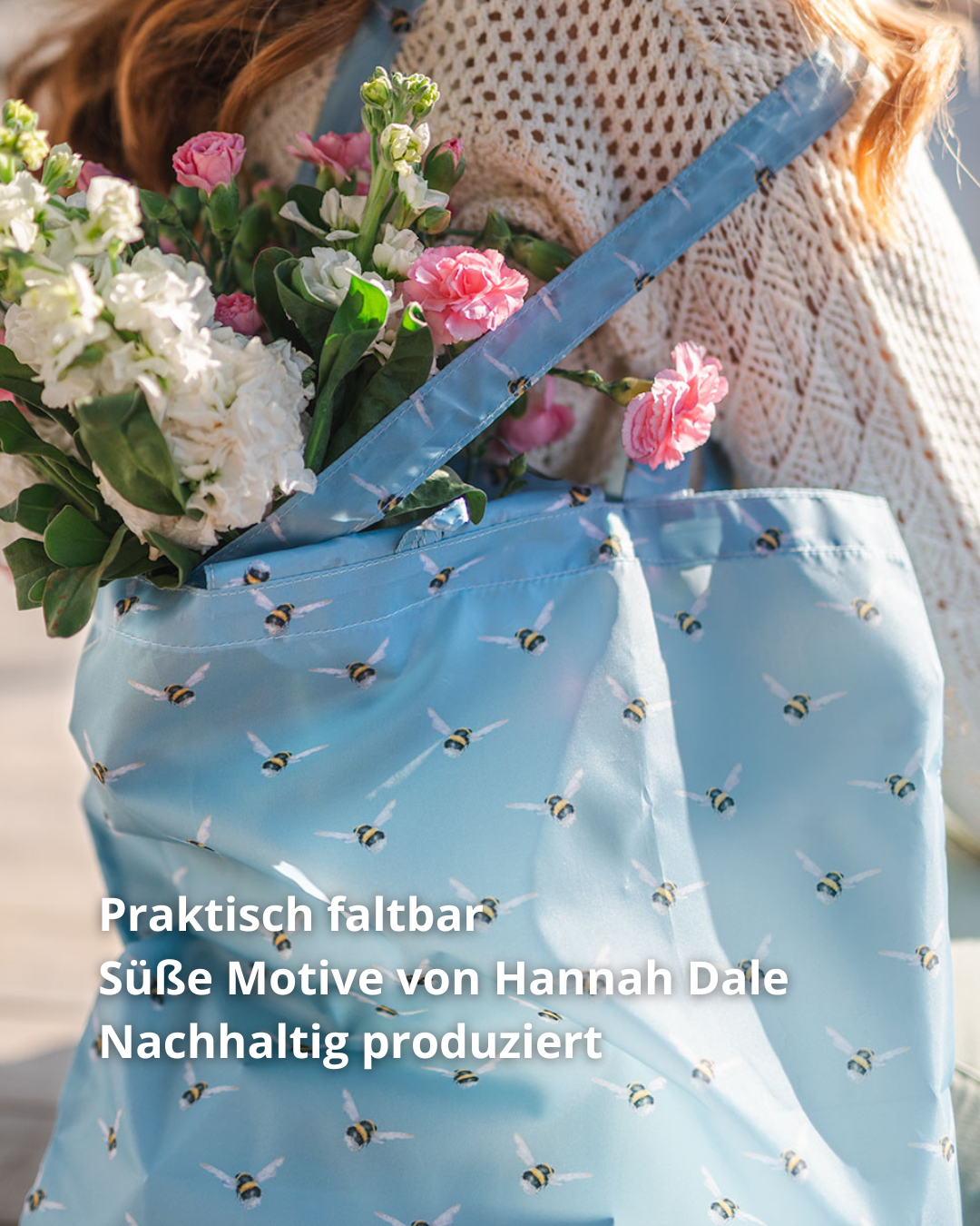 Hellblaue Einkaufstasche Busy bee von Wrendale Designs in Benutzung beim Transport von rosafarbenen und weißen Blumen. Gut zu erkennen sind die von Hannah Dale liebevoll gestalteten Hummeln.