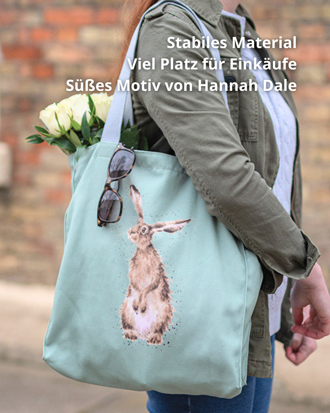 Hellgrüne Hasen-Einkaufstasche von Wrendale Designs getragen von einer Frau. Das Motiv ist ein aufrecht stehender Hase welcher neugierig in die Ferne guckt.  An der Tasche hängt eine Sonnenbrille und es hängen weiße Tulpen raus. 