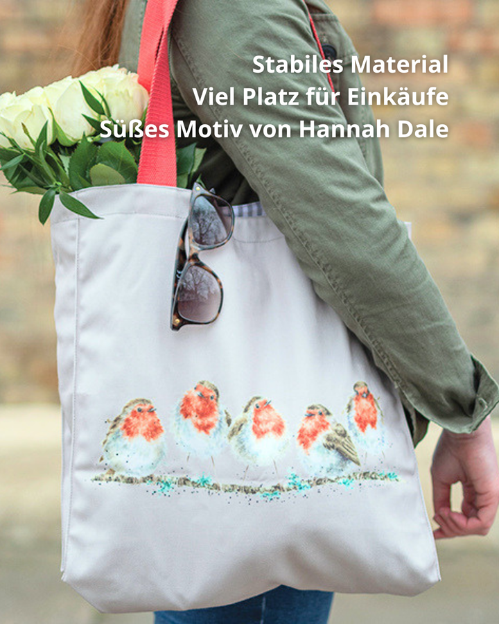 Rotkehlchen Einkaufstasche von Wrendale Designs getragen von einer Frau in blauen Jeans und grünem Oberteil. Die Tasche ist hell Grau und hat viele kleine unterschiedlich stehende Rotkehlchen als Motiv. Die Tasche ist gefüllt mit weißen Blumen.