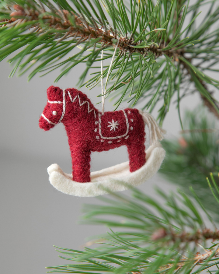 Weihnachtlicher Filzanhänger "Schaukelpferd" von Gry &  Sif in kräftigem rot mit weiß gestickten Highlights. Hier von einem Nadelholzzweig hängend.