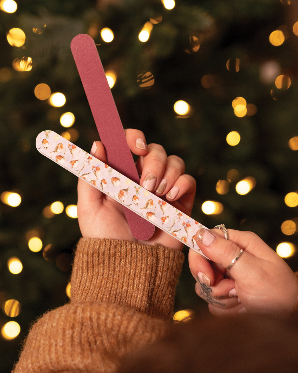 Hände halten Rotkehlchen-Nagelfeile von Wrendale Designs vor Weihnachtsbaum.