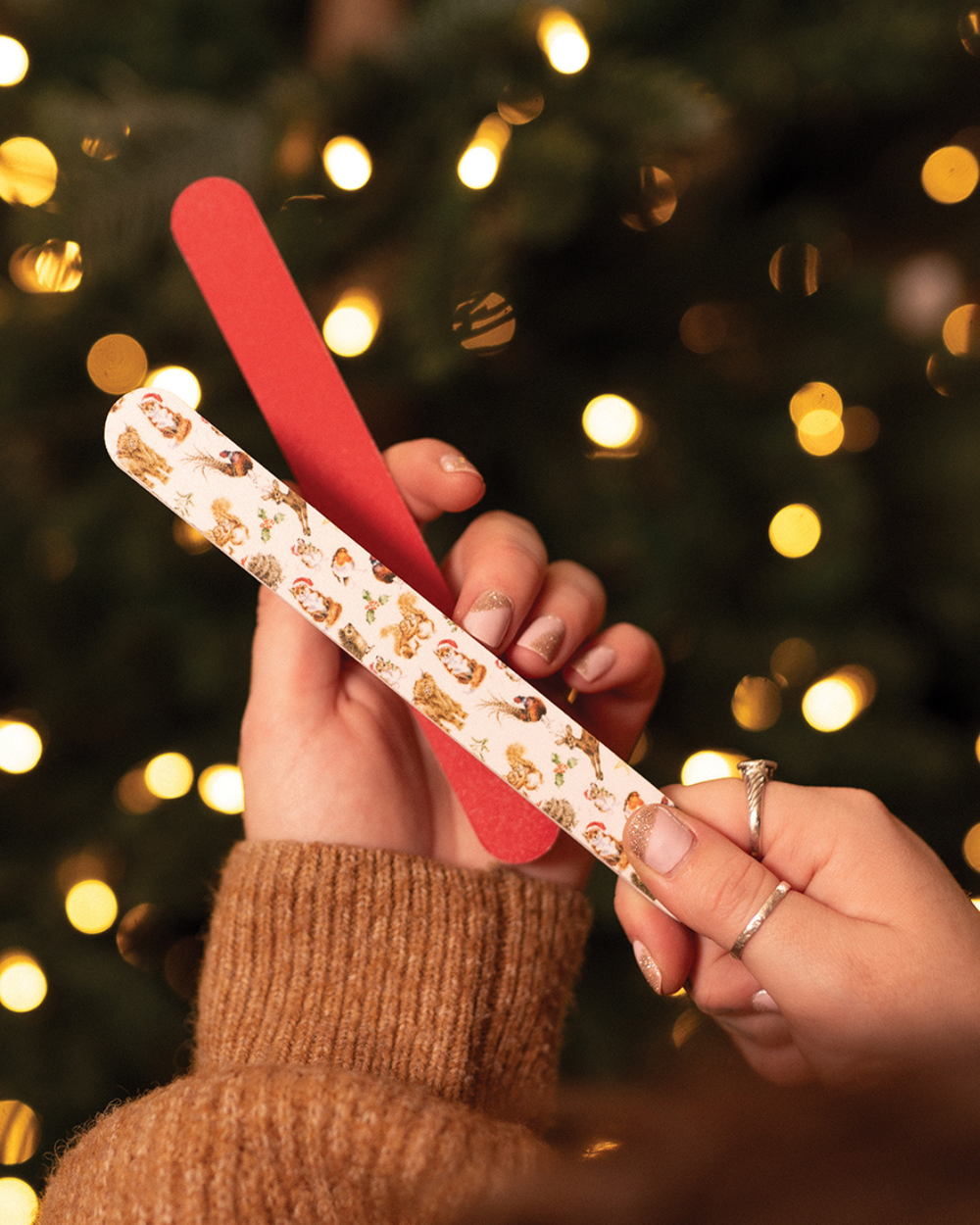 Hände halten Nagelfeile „Winter Woodland“ von Wrendale Designs vor Weihnachtsbaum.