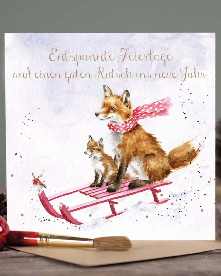 Fröhliche Weihnachtskarte mit Schlittenfüchsen von Wrendale Designs auf einem Tisch.