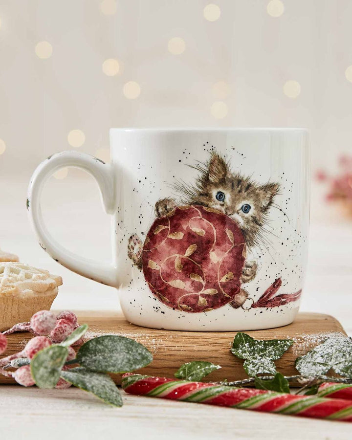 Die Katzen Weihnachtstasse von Wrendale Designs ist auf einem Holzbrettchen mit Tannengrün und Süßigkeiten dekoriert.