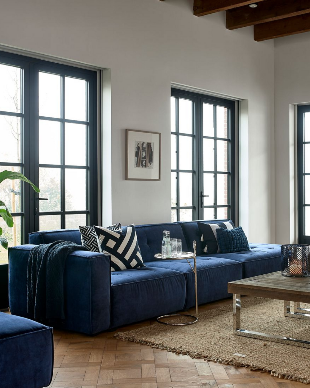 Wohnzimmer mit blauem Sofa, dekoriert mit dem Yacht Club Graphic Kissenbezug von Rivièra Maison im maritimen Design.