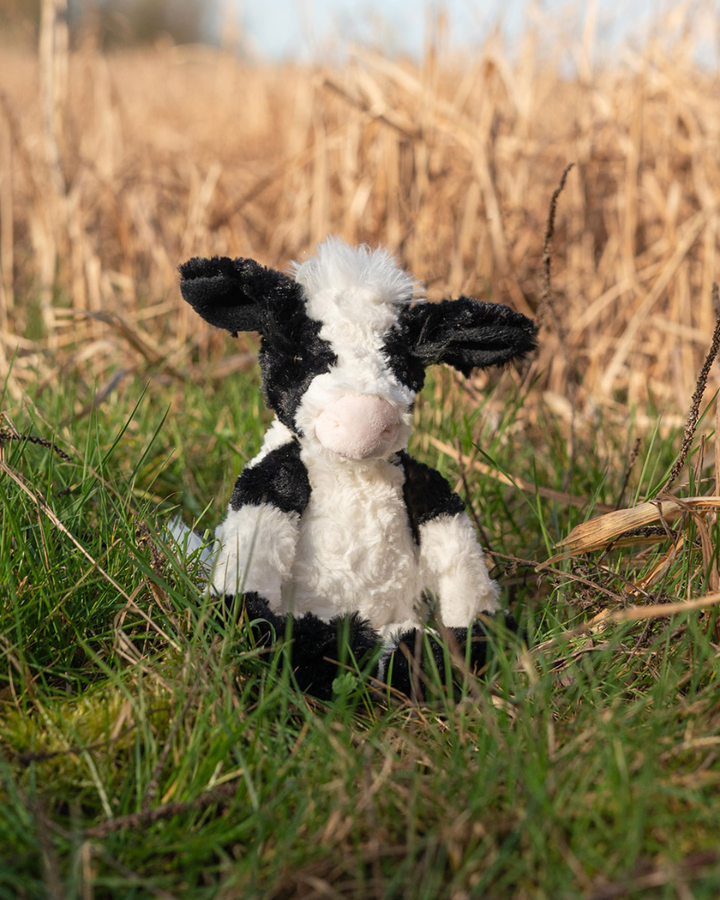 Kuh Schlüsselanhänger "Mathilda" von Wrendale Designs. Die Kuh hat das typische schwarz/weiß Muster. Der Schlüsselanhänger sitzt auf einer grünen Wiese.
