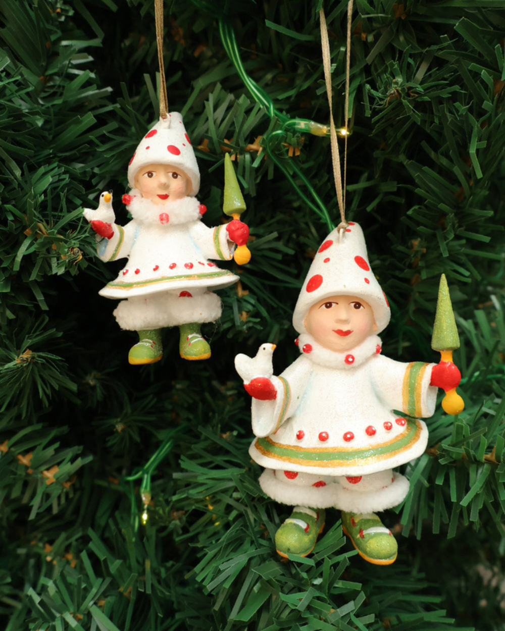 Zwei Größen der "Blitzens Elf" Krinkles hängen an einem Tannenbaum. Zu sehen sind 2 größtenteils weiß bekleideten Elfen mit roten Pünktchen. In den Händen halten sie jeweils einen kleinen Vogel und ein kleinen Tannenbaum Stab.