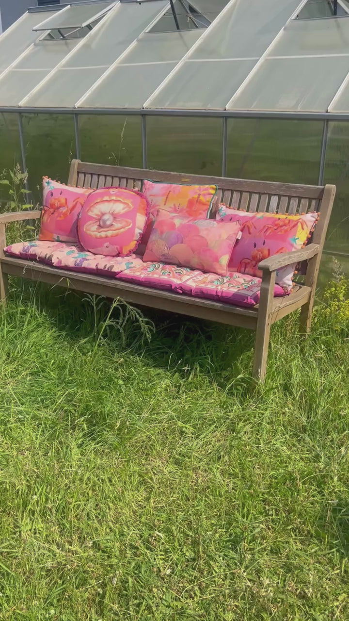 Pinke Outdoor Kissen auf einer Bank im Grünen vor einem Gewächshaus dekoriert.