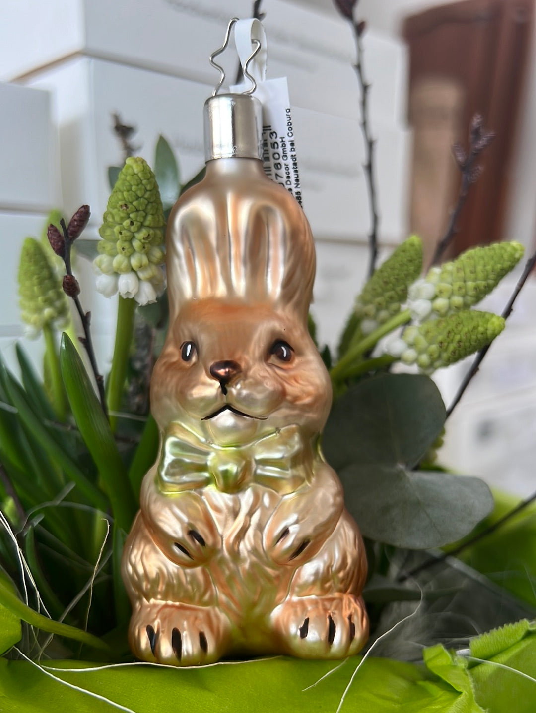Handgefertigter Hase mit Schleife von Inge Glas. Der hellbraune Hase mit aufgestellten Löffeln trägt eine kleine grüne Fliege.