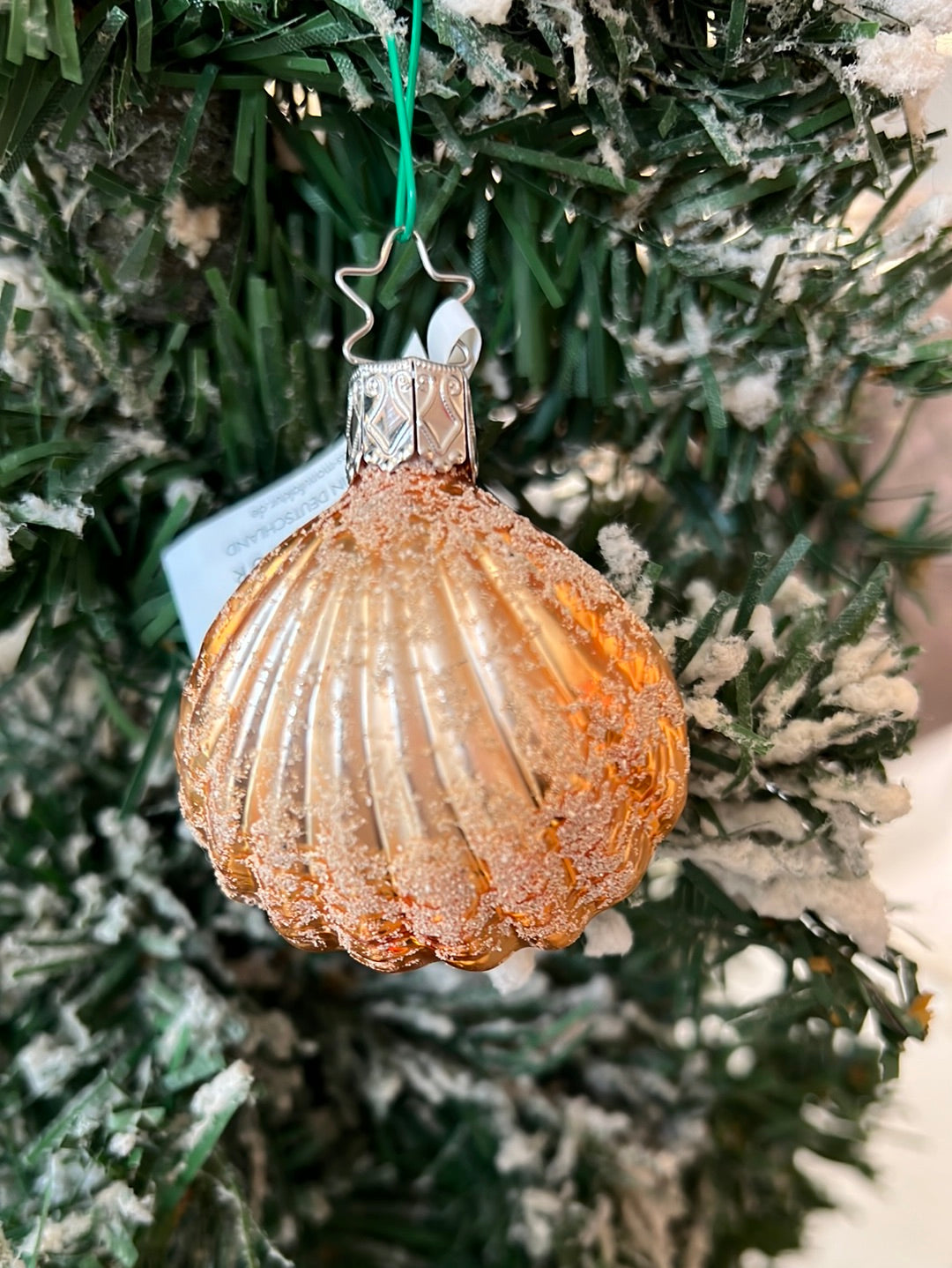 Hübscher, handgefertigter  Muschelanhänger von Inge Glas in orange-gold mit vielen Glitzer Highlights. Hier in einem winterlichen Tannenbaum hängend.