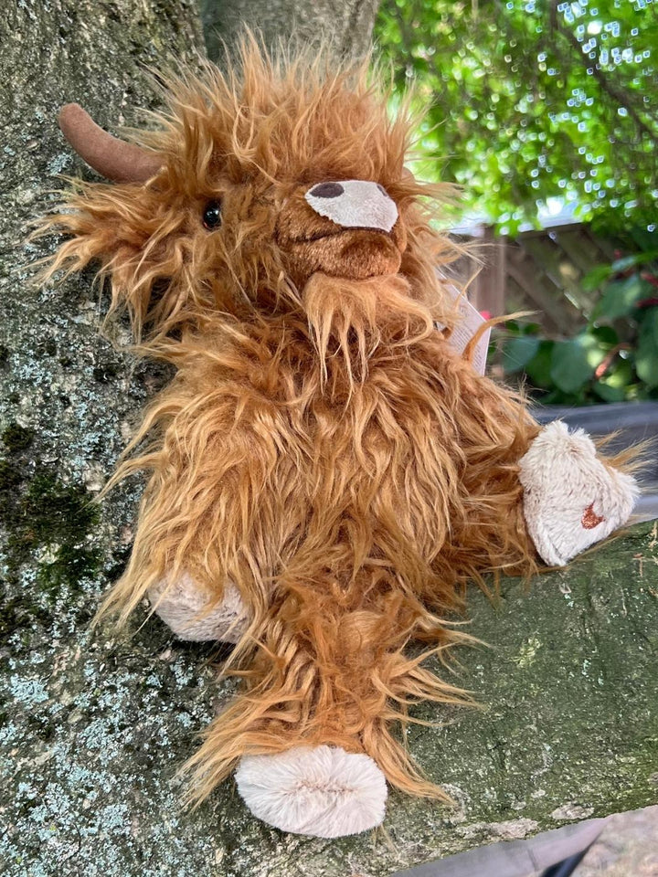 Das Wrendale Designs Kuscheltier Highlandrind Gordon in braun sitzt auf einem Baum.